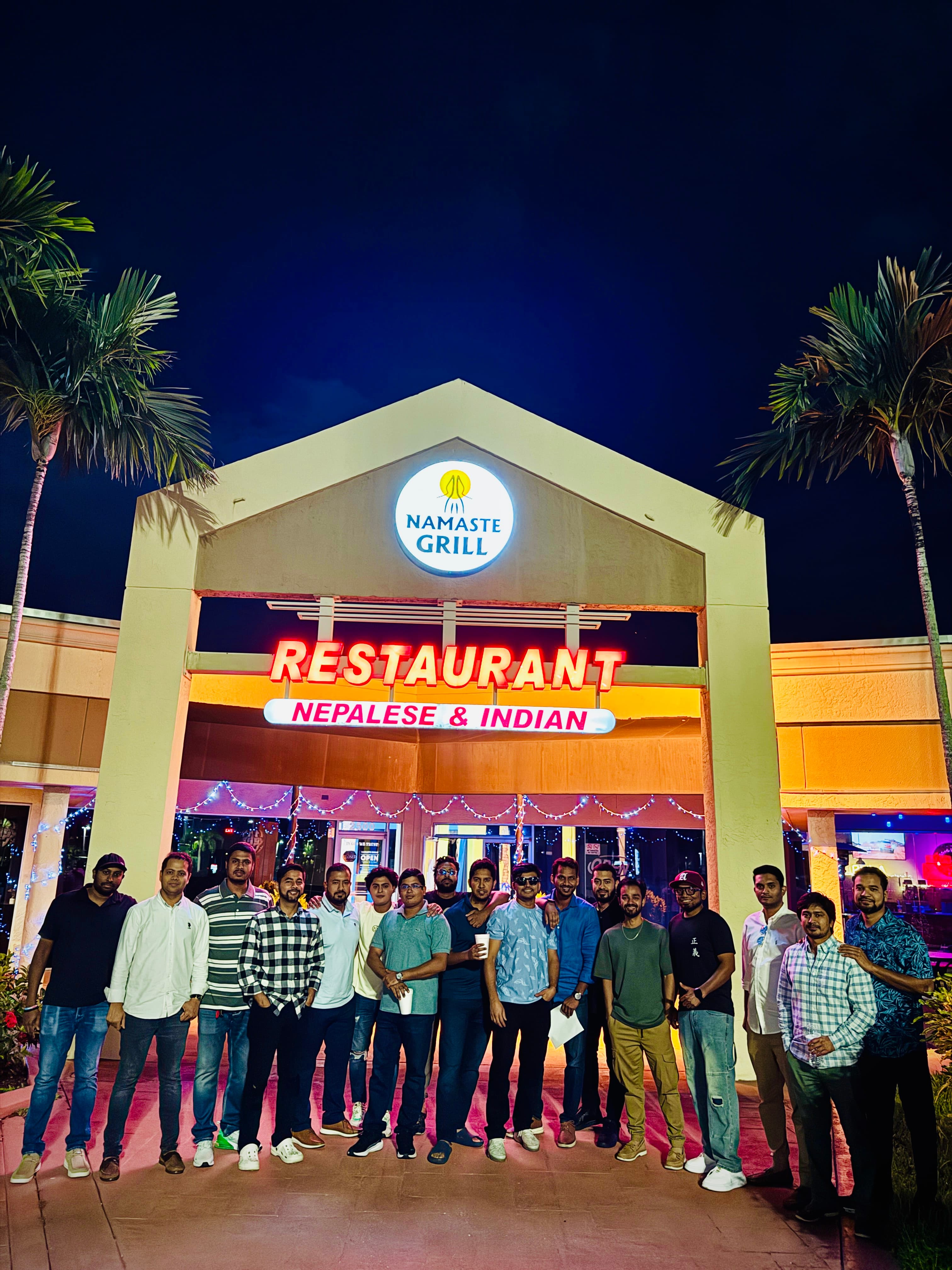 A large party of guests outside the restaurant at night, under the lit sign